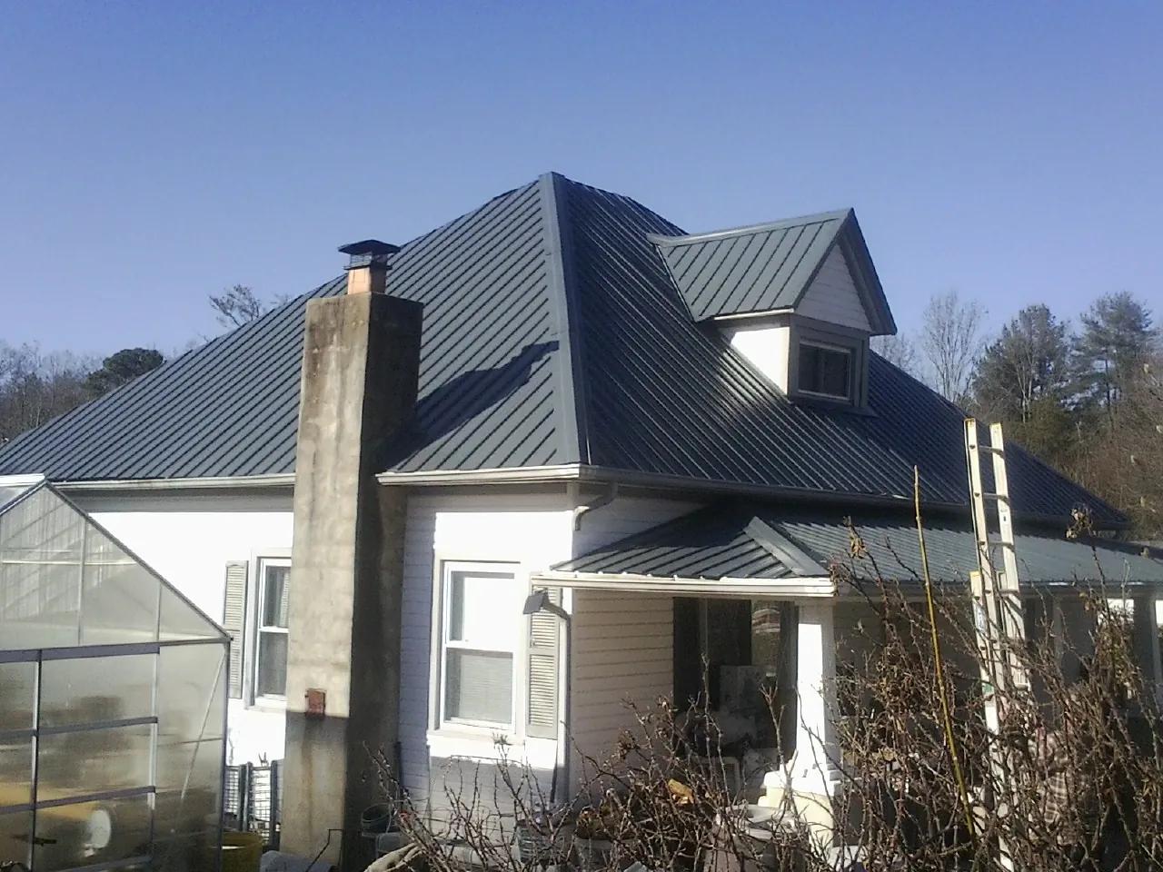 Dark blue standing seam metal roof on a white farmhouse with dormer — Slate & Tile Roof Repair by Roofing Brothers in Deer Creek