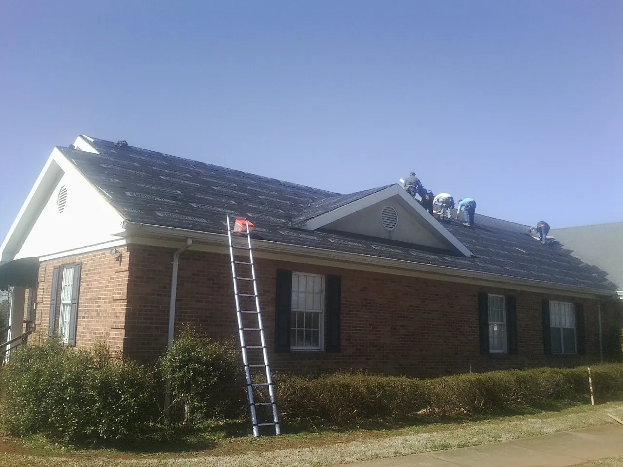 Crew tearing shingles off a brick ranch roof with a ladder set — Metal Roof Repair work by our crew in Deer Creek