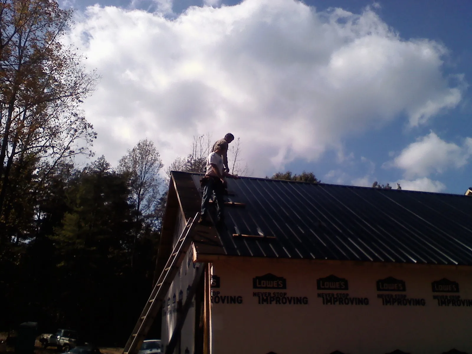 Roofer fastening dark metal panels high against a cloudy sky, from a Roof Inspection job in Deer Creek