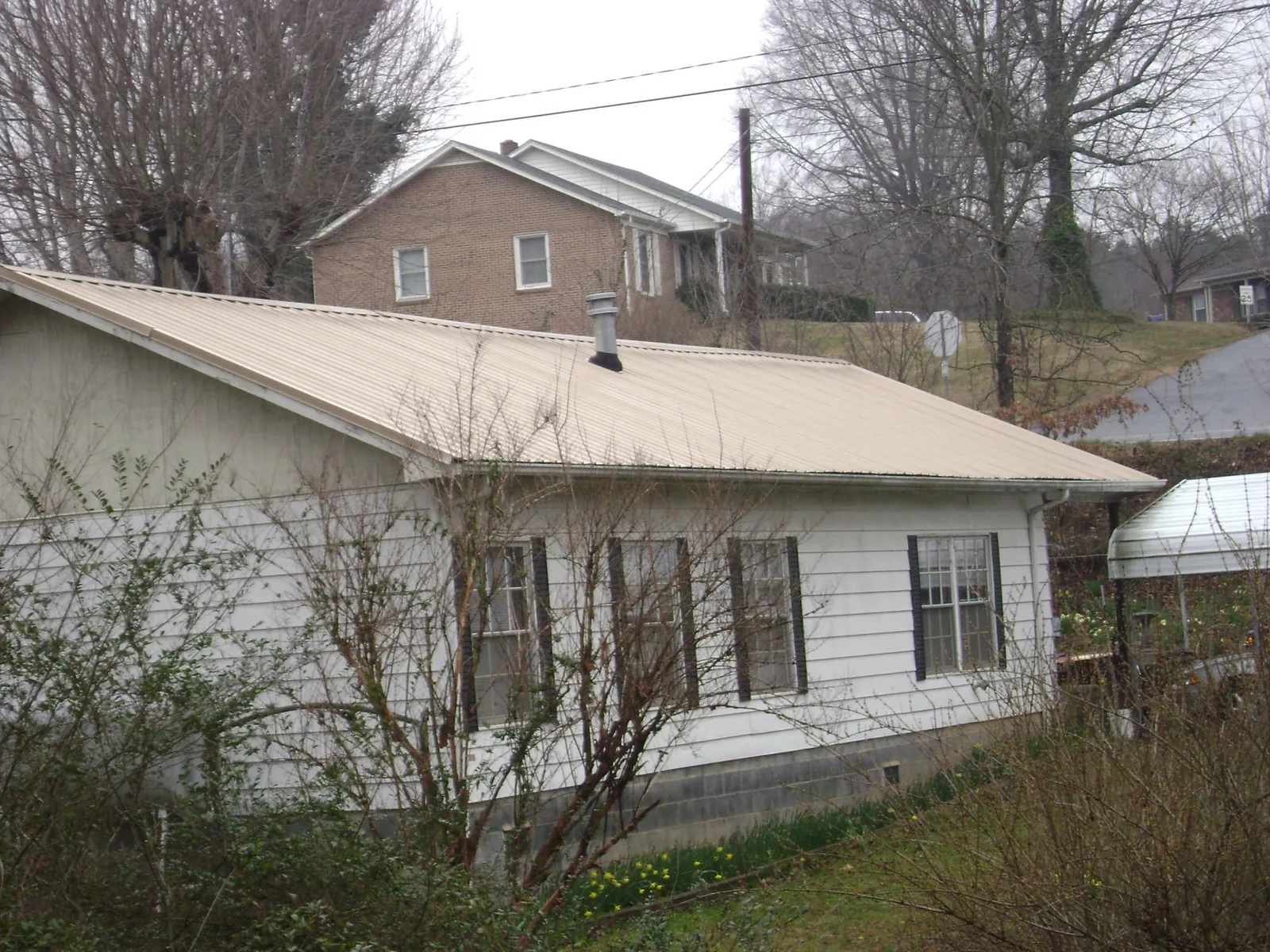 Tan metal roof on a white sided house set into a hillside — Commercial Roofing by Roofing Brothers in Deer Creek