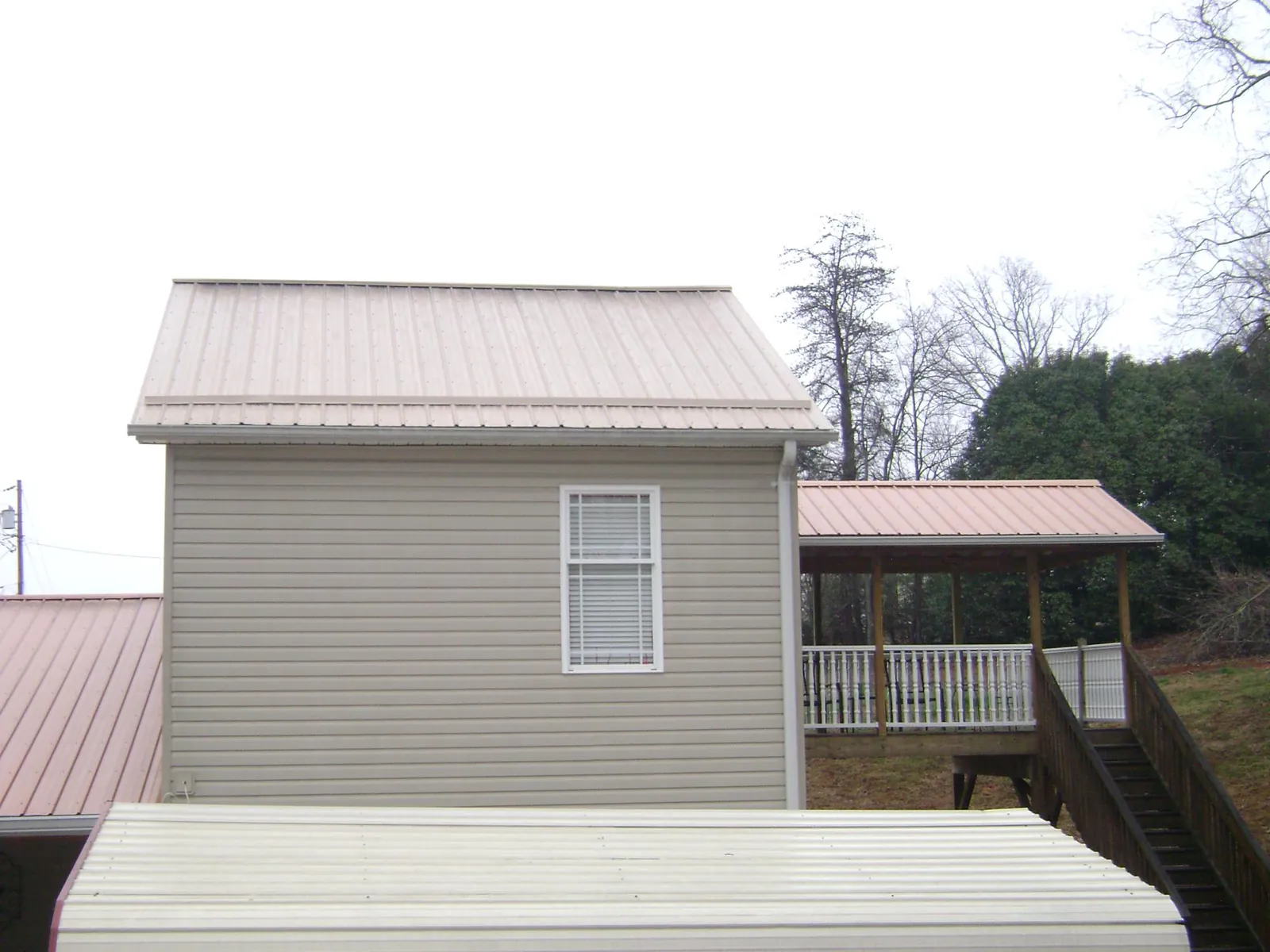 Tan metal roofs on a two story addition and attached porch, from a Roof Replacement job in Deer Creek